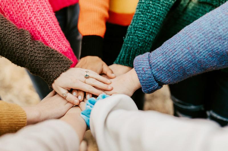 A circle of women in colourful knitwear put their hands together. Photo: Hannah Busing / Unsplash